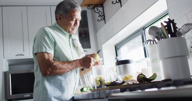 Elderly man engaged in chopping vegetables in a bright, modern kitchen. Could be used for themes about healthy living, senior life, domestic activities, and cooking skills.