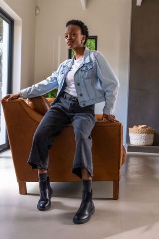 African american woman sitting on leather armchair wearing denim jacket and ankle boots
