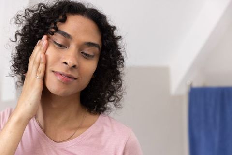 Non-binary person practicing gentle skincare and self-care in soft-lit bathroom portrait