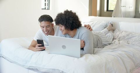 Smiling Couple Browsing Devices Together in Cozy Bedroom