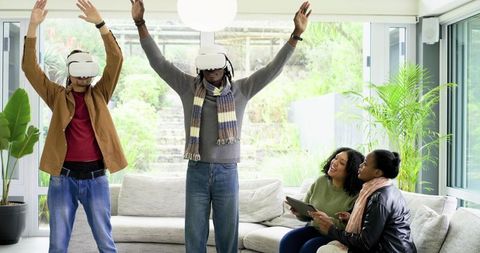 Friends playing virtual reality games and cheering in modern living room with VR headsets