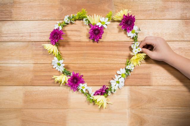 Hand preparing a tropical flower garland arranged in heart shape on wooden board