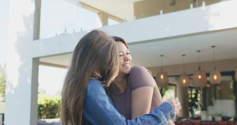 Two Friends Embracing on Sunny Patio Sharing Joy and Warm Welcome at Contemporary Home