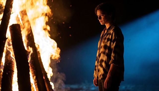 Woman standing beside bonfire under blue night light, cinematic campfire portrait