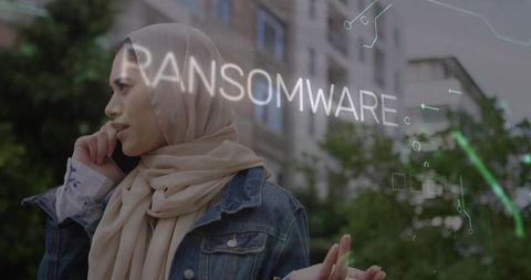 Woman wearing hijab calling on phone with ransomware alert overlay in urban courtyard