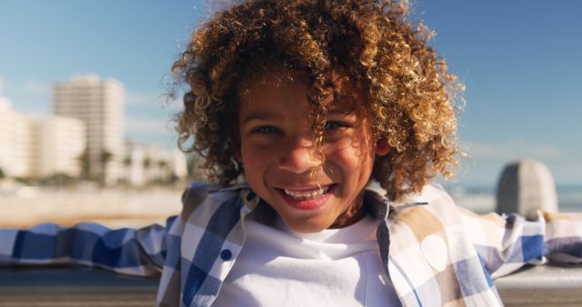 Child celebrating a sunny day at the beach with buildings and an ocean backdrop. Effective for advertisements, family-oriented content, and vacation promotions.