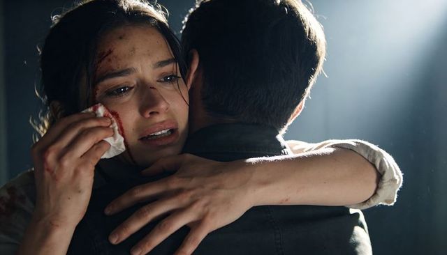 Injured woman embracing partner, crying and holding bloody tissue in dramatic backlight
