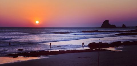 Sunset Silhouettes on Rocky Beach with Calm Waves and Vivid Orange Purple Sky