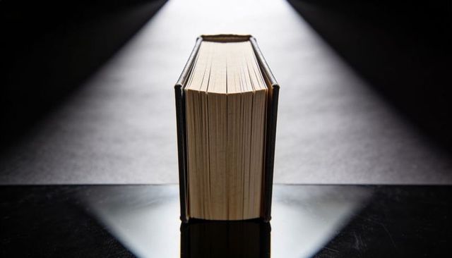 Standing vintage hardcover book under dramatic spotlight on reflective black surface
