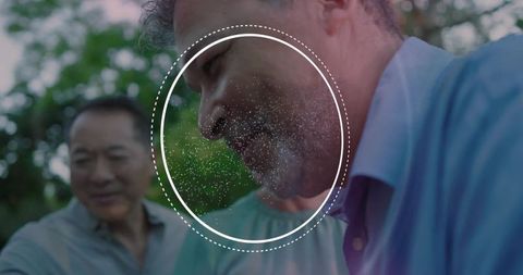 Bearded man smiling in outdoor gathering with white circular overlay and soft bokeh