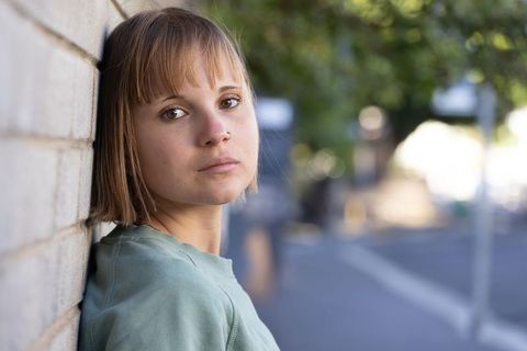 Pensive young woman leaning on brick wall urban street portrait mint sweatshirt soft light