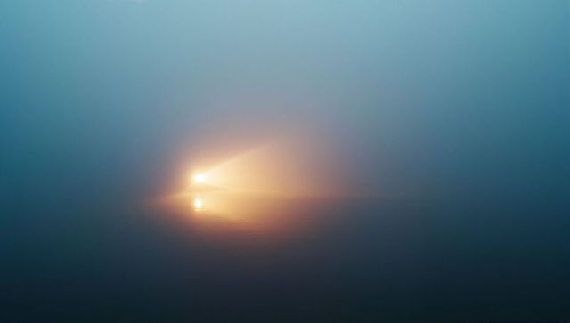 Mysterious fog-diffused light orb reflecting on misty water