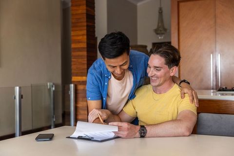 Smiling interracial couple reviewing and signing home documents at modern kitchen table