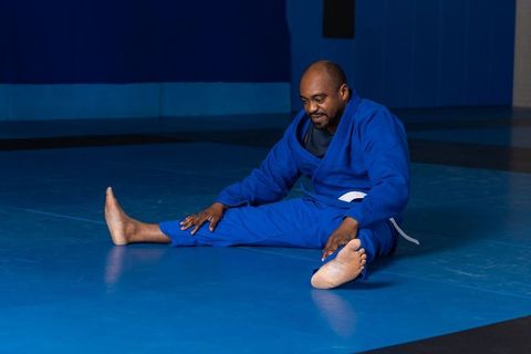 Senior man in blue gi stretching in dojo for flexibility and fitness