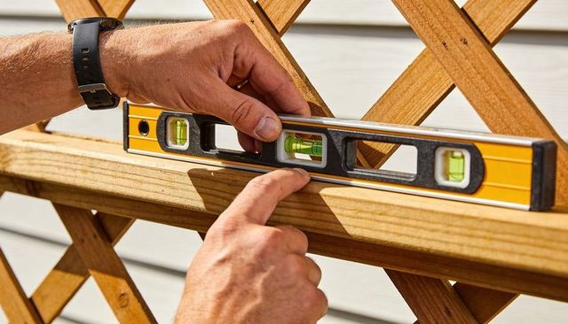 Male hands adjusting spirit level on wooden trellis ensuring straight alignment for diy
