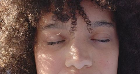 African american woman closing eyes under dappled sunlight, curly hair close-up portrait