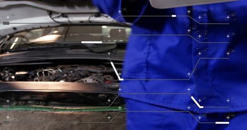 Auto technician inspecting engine wiring wearing blue coveralls with diagnostic overlay
