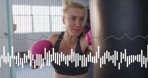 Mid-adult woman boxing workout pink gloves hitting heavy bag gym studio waveform overlay