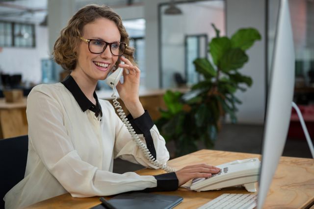 Woman talking on landline phone at desk in office