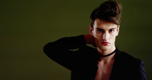 A young Caucasian male model poses confidently against a green background, with copy space. His intense gaze and stylish attire suggest a fashion or advertising shoot.