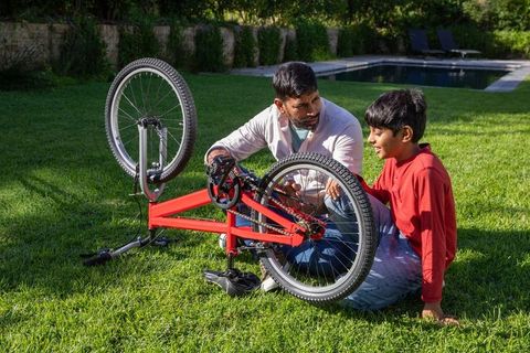 Father teaching son bicycle repair outdoors by family pool