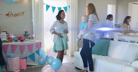 Smiling pregnant woman cradling belly at pastel baby shower with friends and cupcakes