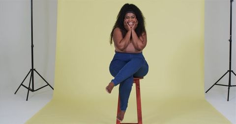 Smiling woman on stool with yellow studio background