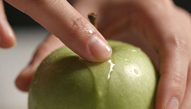 Fingertip pressing juicy green apple with dew droplets closeup for fresh food ads