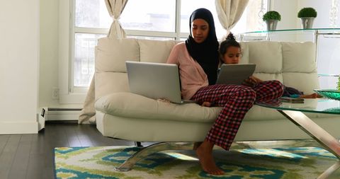 Mother and Daughter Using Laptop and Tablet on Sofa in Living Room