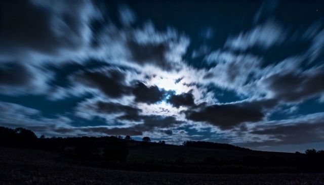Moonlit Night with Dramatic Cloud Motion over Silhouetted Hills and Trees Long Exposure