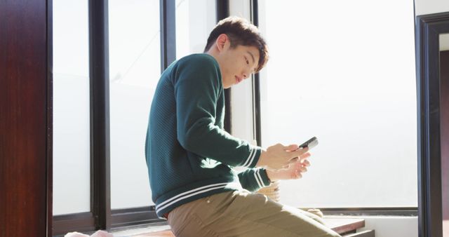 Young Man Using Smartphone Near Large Window on Sunny Day - Download Free Stock Images Pikwizard.com