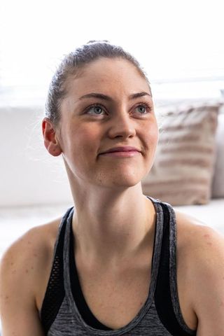 Young woman on sofa smiling and looking upward, calm home wellness portrait