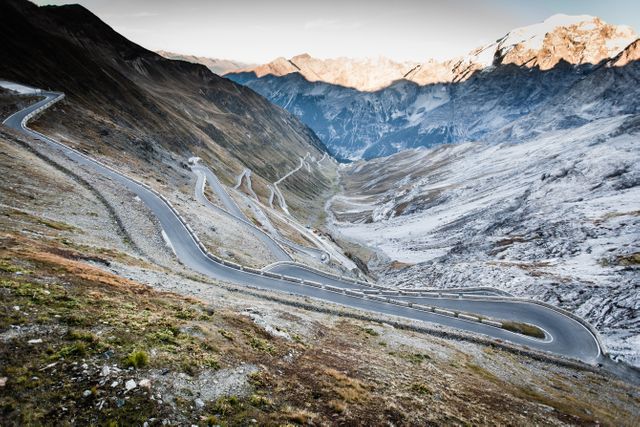 Curved road meandering through snow-capped mountains in autumn offers breathtaking scenery ideal for travel, adventure enthusiasts, and road trip promotions. Use it for travel blogs, adventure websites, or advertisements highlighting scenic drives and mountainous landscapes.
