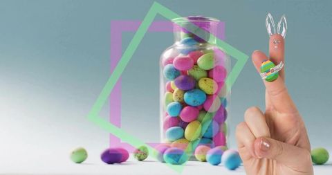 Finger bunny holding painted easter egg beside glass jar filled with speckled pastel candy
