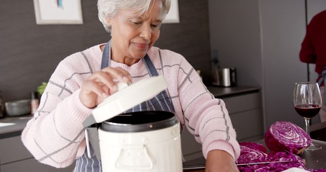 Senior woman wearing apron, chopping purple cabbage and preparing a meal in a modern kitchen. Ideal for use in content about healthy lifestyles for seniors, home cooking, family recipes, or promoting dietary health and wellness. Suitable for illustrating content related to aging, senior living, and domestic life.