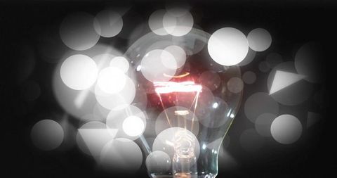 Glowing incandescent bulb with exposed tungsten filament and geometric bokeh reflections