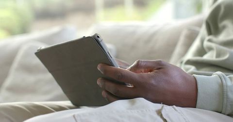 African American Man Holding Tablet on Sofa Using Touchscreen in Cozy Living Room