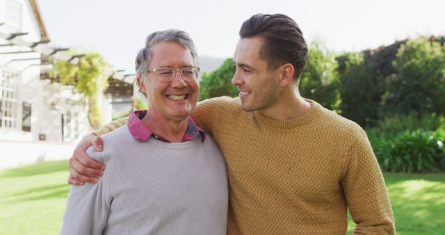 Father and son hugging and smiling outdoors in a sunny garden. Suitable for topics like family bonds, happiness, Father's Day, intergenerational relationships, and quality time spent with loved ones. Ideal for use in advertisements, websites, and social media posts focused on family values and emotional connections.