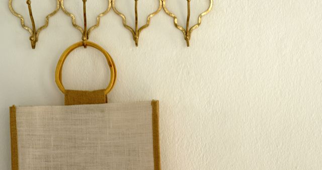 A minimalist wall decor features a simple canvas bag hanging beneath elegant golden wall sconces, with copy space. The neutral tones and clean lines create a serene and sophisticated atmosphere.