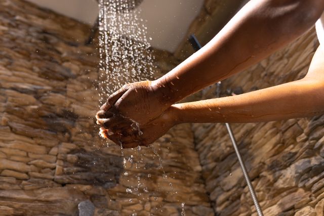 Low angle view of cropped hands of african american young woman cupping shower's water in bathroom. Unaltered, hygiene, routine, lifestyle, self care, bathing, home.