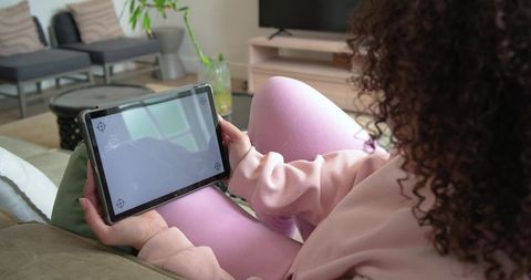 African american woman holding tablet with blank crosshair screen on sofa for app mockup