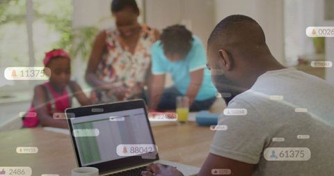 Man working on laptop at family table while children studying with notification overlays