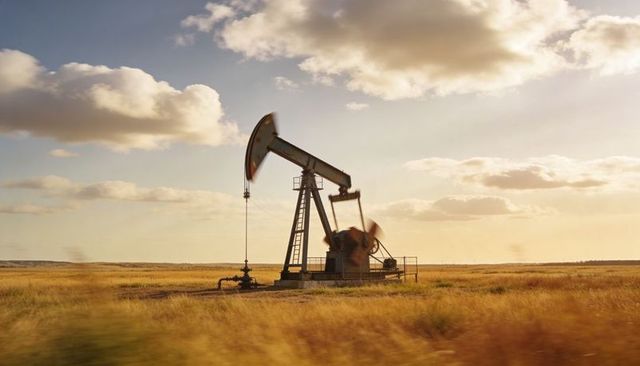 Pumpjack pumping on golden prairie at sunset with wellhead and ladder