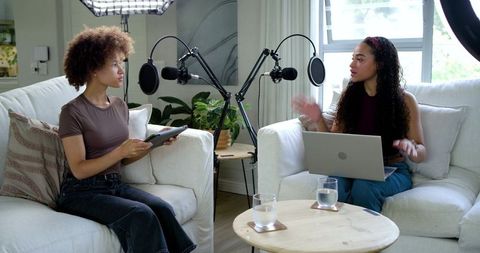 African american cohosts recording podcast on sofas with microphones and laptop at home
