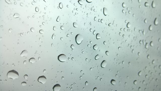 This image shows multiple water droplets settled on a glass window, creating a textured look typical of rainy days. Useful for conveying concepts related to weather, rain, and moisture. Ideal for blog posts about weather topics, setting a rainy atmosphere, or promotional materials for window cleaning products.