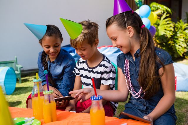 Happy children using mobile phone while sitting at table during birthday party