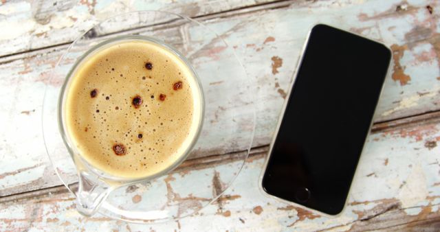 A cup of freshly brewed coffee sits next to a smartphone on a rustic wooden table, with copy space. Perfect for a concept on morning routines or the blend of technology with daily life.