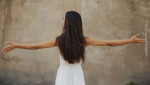 Woman in white dress stretchingly facing away outdoors