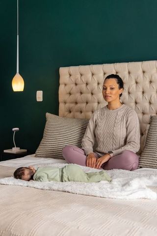 Mother watching newborn resting on fluffy blanket in cozy tufted bedroom
