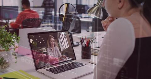Asian woman attending remote video meeting on laptop in open-plan office for teamwork